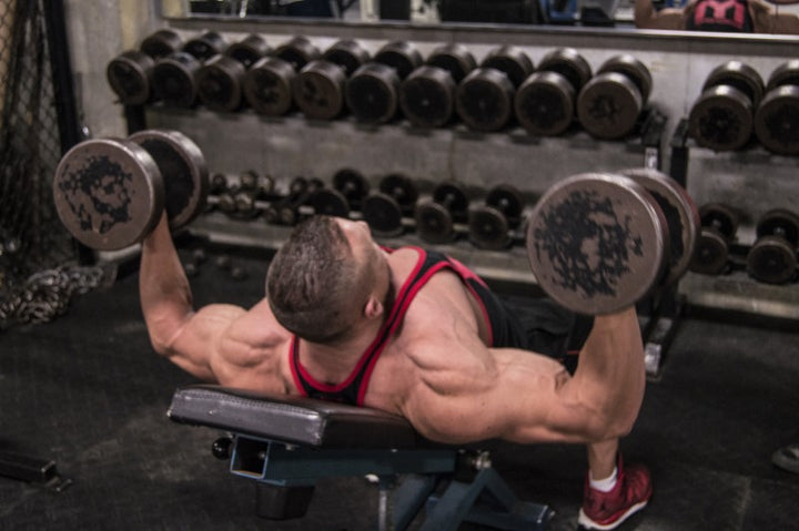 Marc Lobliner lying on a flat bench performing dumbbell flys with a controlled stretch across the chest on chest day