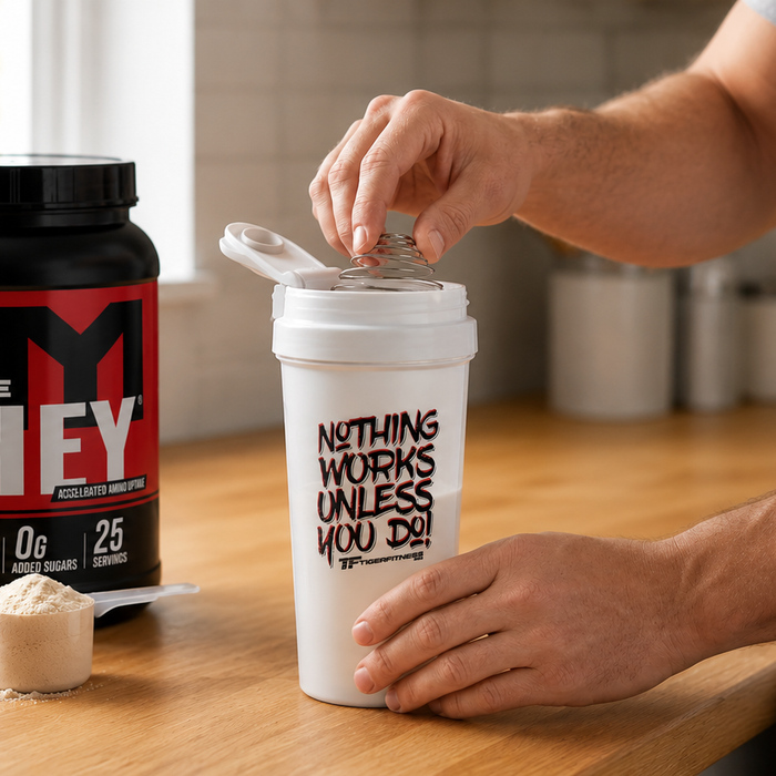MTS Nutrition Machine Whey protein powder with a Tiger Fitness shaker as an athlete prepares a protein shake on a kitchen countertop.
