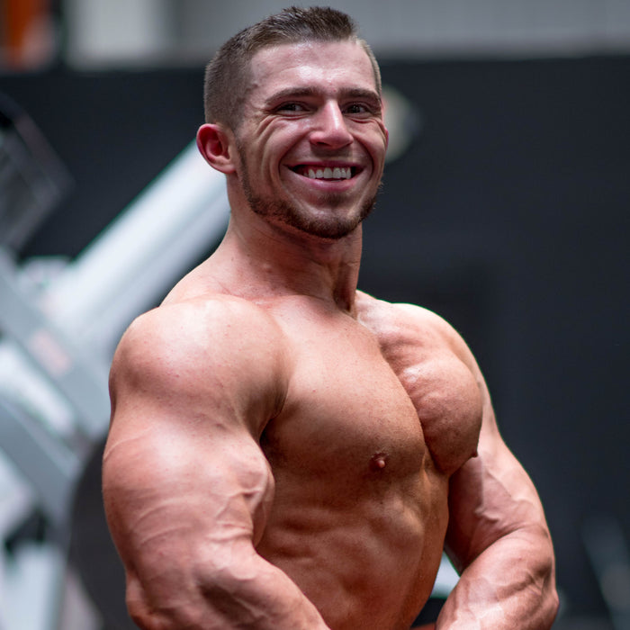 Zach Buckeye in a front physique pose in the gym, chest and torso lit from above, no equipment in frame.