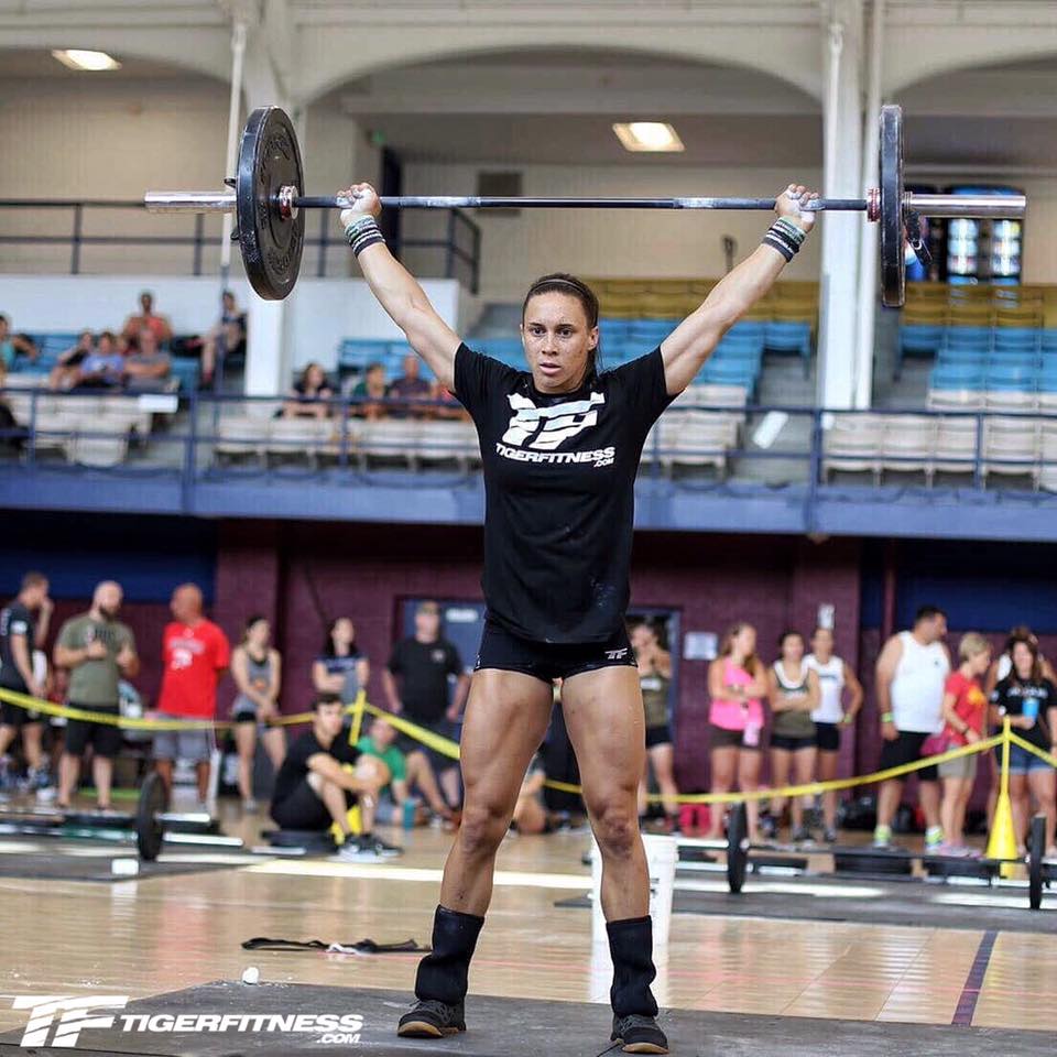 Athlete locking out a barbell overhead with arms extended and ribs down during a standing overhead press in training