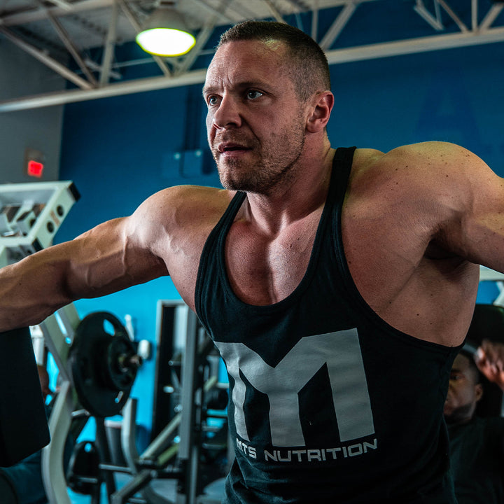 Marc Lobliner holding dumbbells at the top of a lateral raise, elbows slightly bent and wrists level with the shoulders