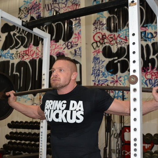Marc Lobliner raising a pair of dumbbells out to the sides in a strict lateral raise during a shoulder focused workout