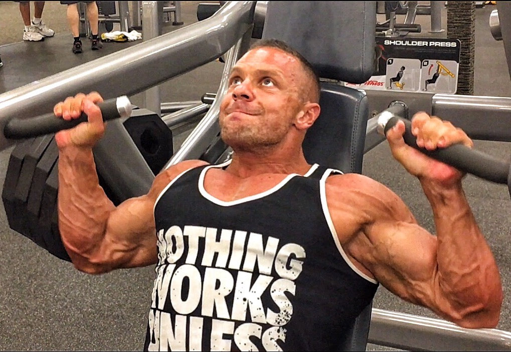 Marc Lobliner pressing overhead on a machine shoulder press during a dedicated shoulder day in a five day body part split