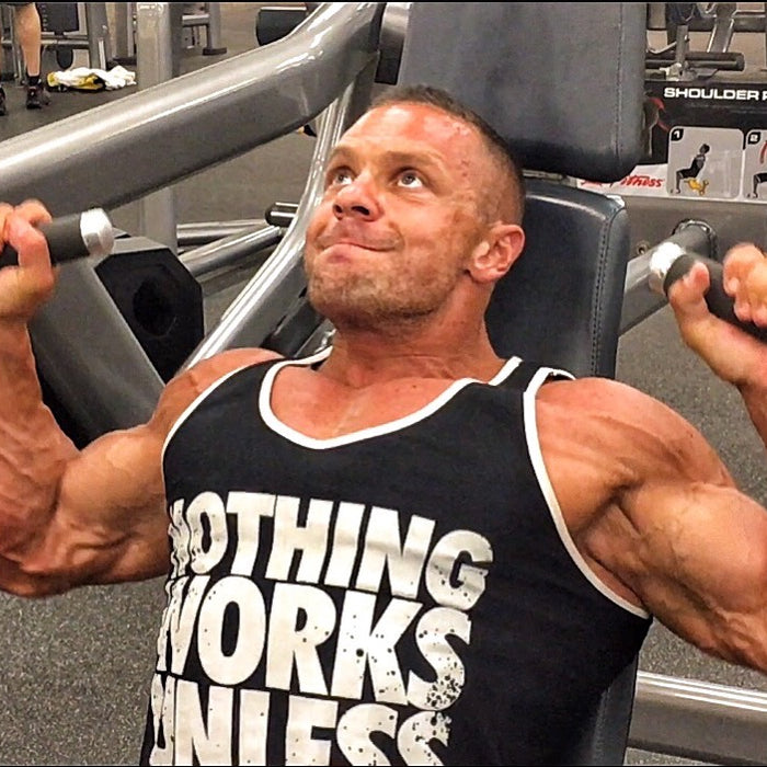 Marc Lobliner pressing overhead on a machine shoulder press during a dedicated shoulder day in a five day body part split