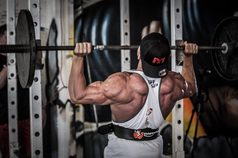 Marc Lobliner hanging from a fixed pull-up bar mid rep, lats loaded near the top of a wide grip pull-up.