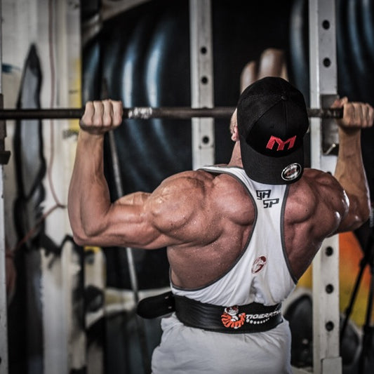 Marc Lobliner hanging from a fixed pull-up bar mid rep, lats loaded near the top of a wide grip pull-up.