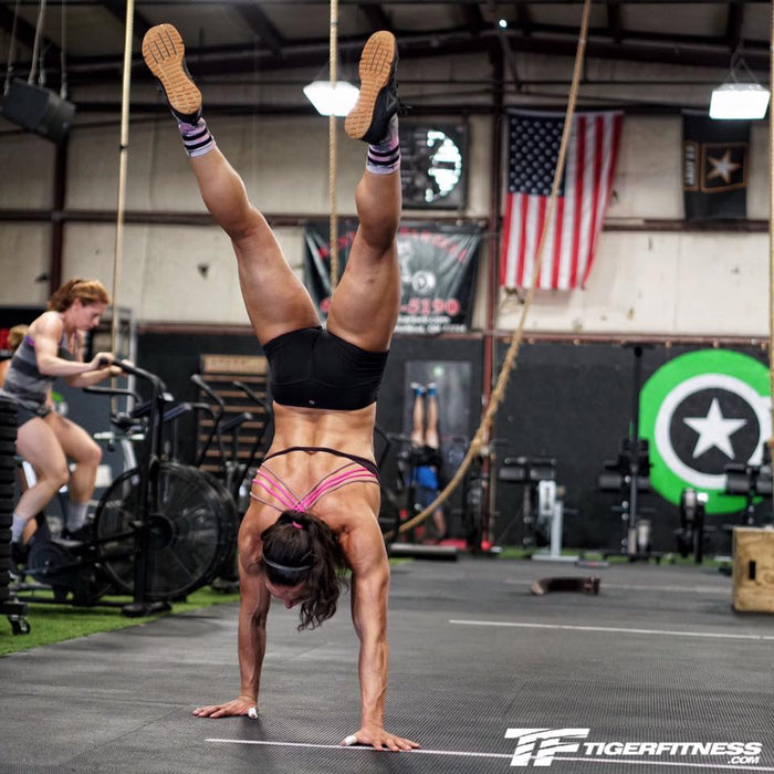 Athlete inverted in a handstand walking across a training floor on her hands, body stacked over her shoulders and legs overhead