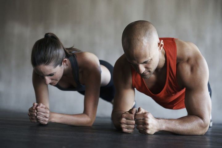 Group of athletes holding a forearm plank in a row on a gym floor, hips level and bodies held in straight lines