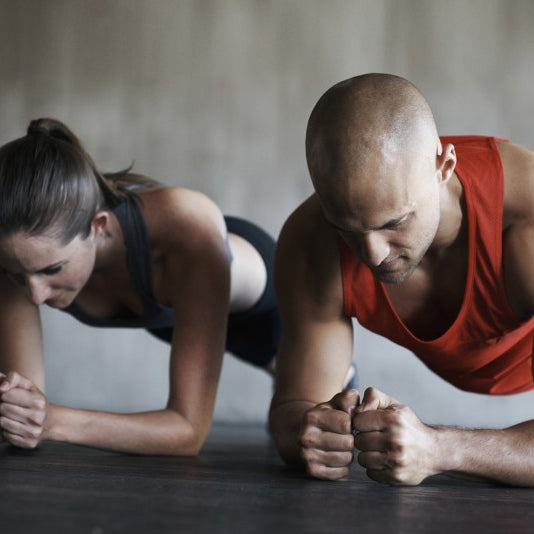 Group of athletes holding a forearm plank in a row on a gym floor, hips level and bodies held in straight lines