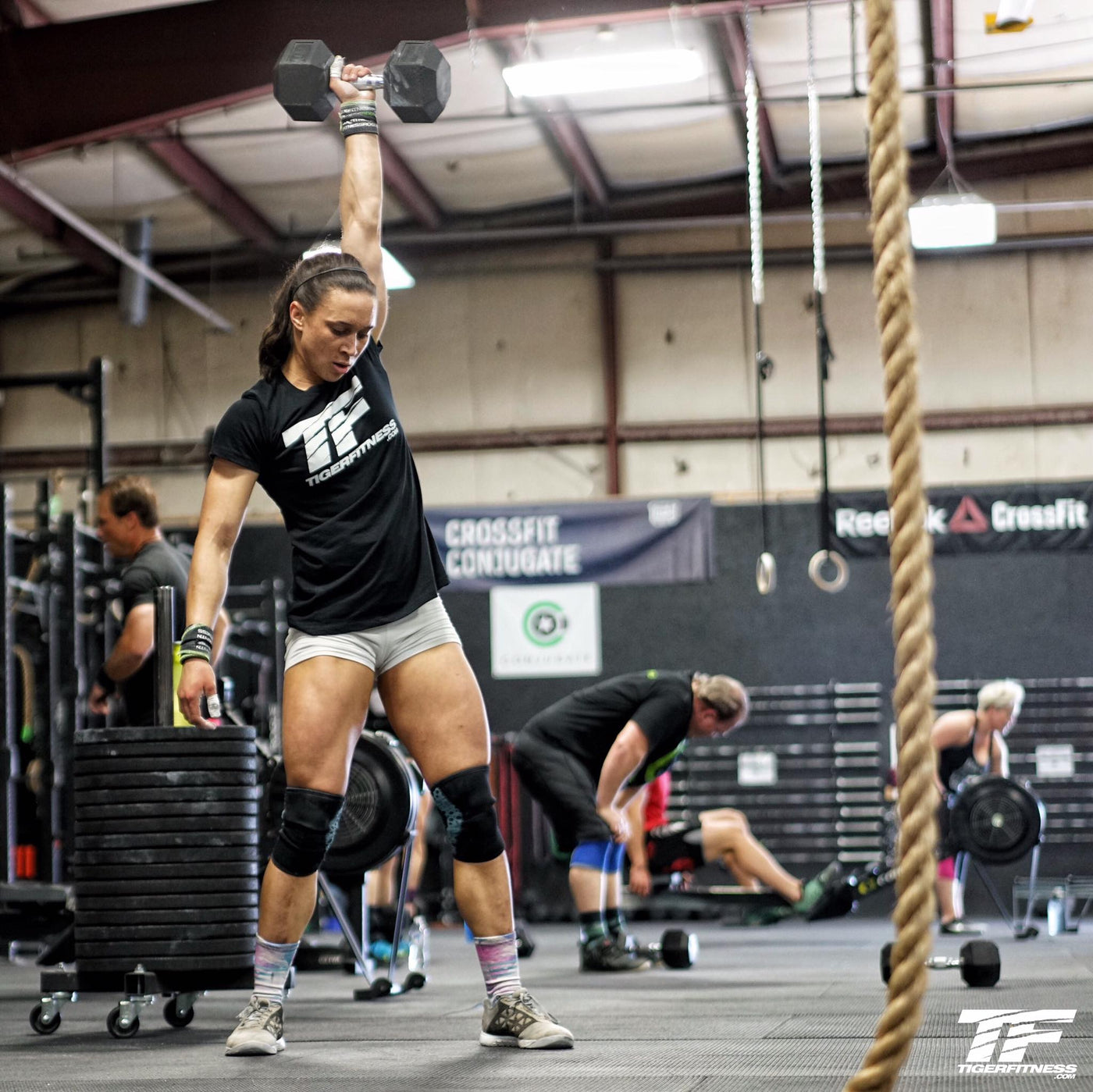 Amanda pressing a single dumbbell overhead with a braced core during a full body strength session for women in the gym