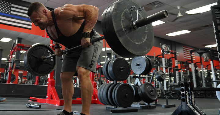 Marc Lobliner performing a single arm dumbbell row in the gym, gripping one heavy dumbbell and driving his elbow back toward his hip.