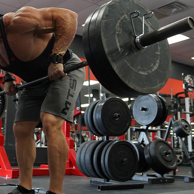 Marc Lobliner performing a single arm dumbbell row in the gym, gripping one heavy dumbbell and driving his elbow back toward his hip.