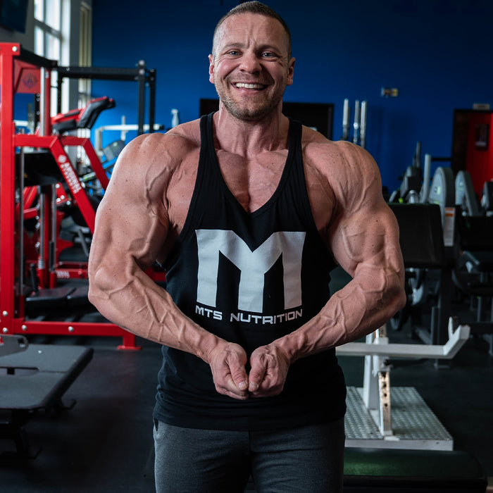 Marc Lobliner standing in a front relaxed bodybuilding pose in the gym, showing the classic proportions this style of training builds
