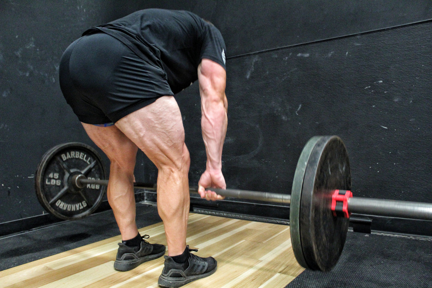 Lifter performing a barbell Romanian deadlift in a gym, bar held at mid-shin with hips pushed back and back flat