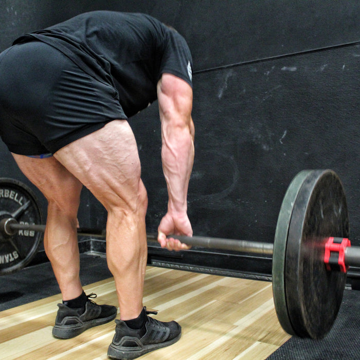 Lifter performing a barbell Romanian deadlift in a gym, bar held at mid-shin with hips pushed back and back flat