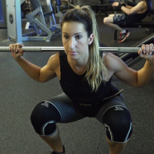 Athlete Kara Corey unracking a loaded barbell for back squats, bar across the upper back and hands set wide