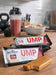 Beverly International UMP Protein Bar in Almond Honey flavor displayed with coffee and gym accessories.